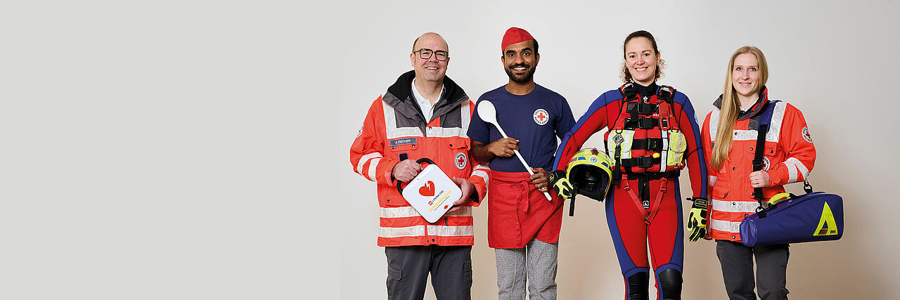Vier ehrenamtliche Einsatzkräfte unterschiedlichen Geschlechtes und unterschiedlicher Hautfarbe stehen nebeneinander und schauen freundlich in die Kamera